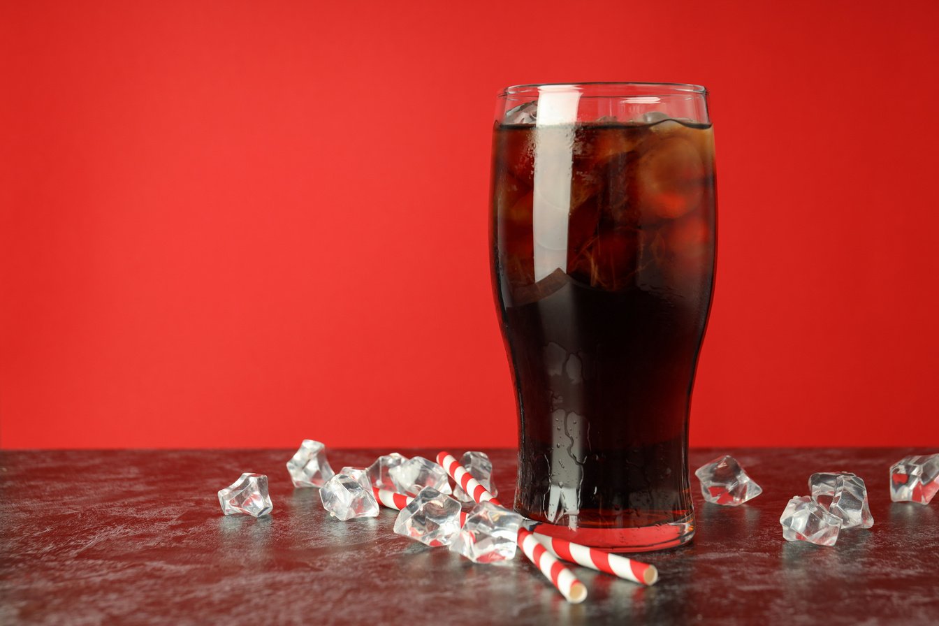 Glass of Cola, Ice and Straws against Red Background